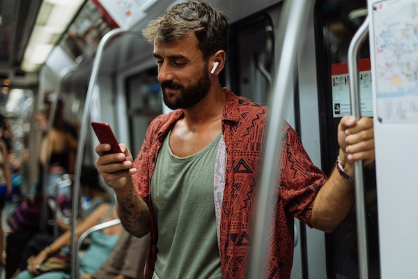 A man holds his phone on the subway, deciding whether he should talk to Siri or keep his mouth shut so we can all ignore each other just a little bit easier.